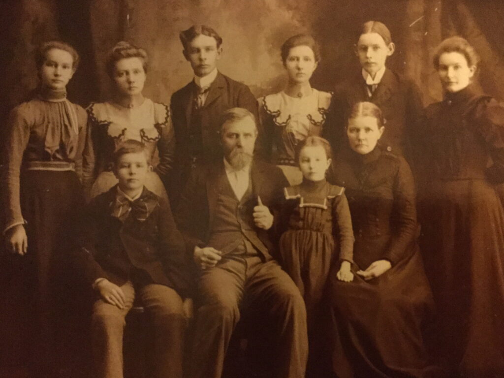 An dark sepia toned photo of a family of eight, with the two oldest and youngest members seated in the front row.